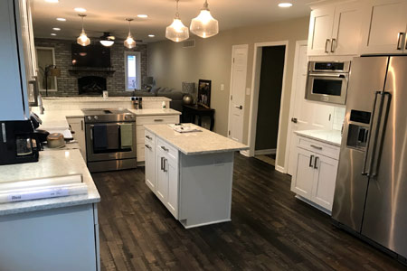 Remodeled kitchen with a centre island, white cabinetry and hardwood flooring